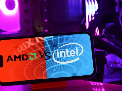 Telefon z logo AMD vs Intel na tle podświetlanego komputera.