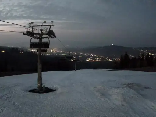 Widok z bukowina ski kamery na ośnieżony stok i nocne światła miasta w oddali.