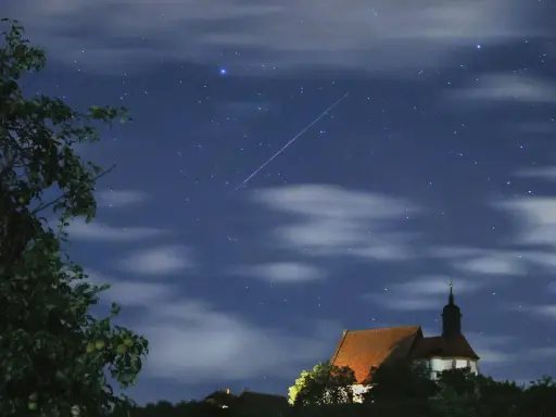 Ein Sternschnuppenregen über einer kleinen Kirche. Man sieht, wann sieht man sternschnuppen, wenn der Himmel klar ist und die Nacht dunkel.