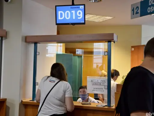Kobieta czeka na odbiór dowodu rejestracyjnego. Na ekranie wyświetla się numer stanowiska D019.