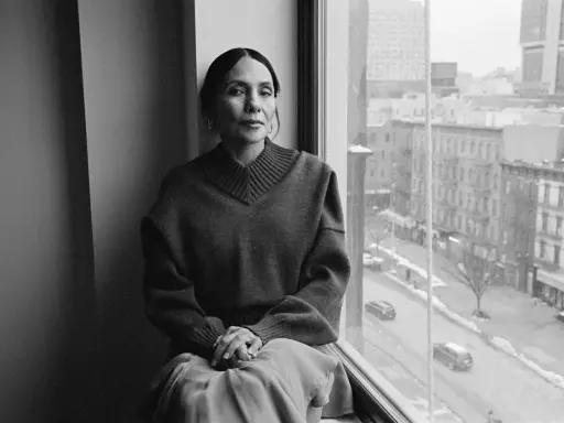 Ming Smith, a woman with her hair pulled back, sits by a window, looking out at a city street.