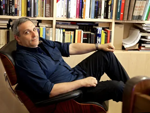 L'autore, circondato da libri, si rilassa su una poltrona. Tra i titoli, si intravede un riferimento a de Giovanni ultimo libro.