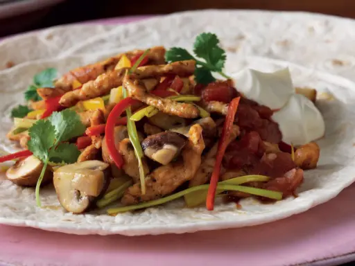 En läcker portion fajitas kyckling med paprika, champinjoner och gräddfil på en tortilla.
