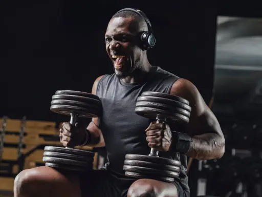 Uomo con cuffie nella palestra gym, solleva pesi con musica per allenamento. Grinta e determinazione.
