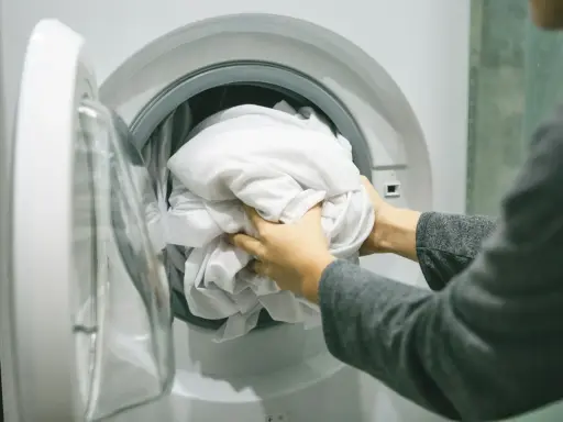 Ręce wkładają białą pościel do pralki. Zastanawiam się, jakie wirowanie w pralce będzie najlepsze dla tej delikatnej tkaniny.