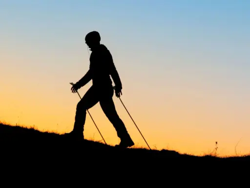 Sylwetka osoby uprawiającej nordic walking na tle zachodzącego słońca. Czy wolisz nordic walking rano czy wieczorem?