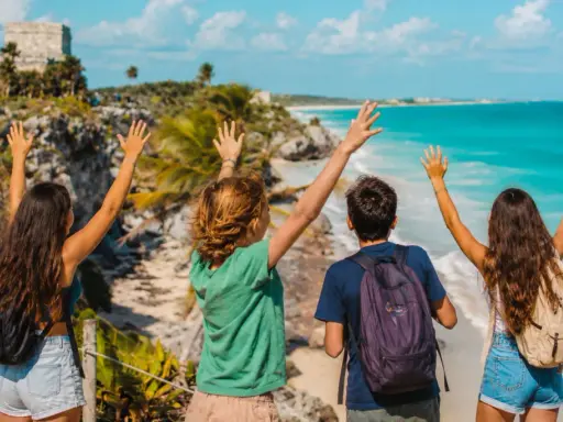 Cuatro jóvenes con mochilas saludan al mar turquesa y las ruinas mayas. ¡Una aventura inolvidable en la Riviera Maya con niños!
