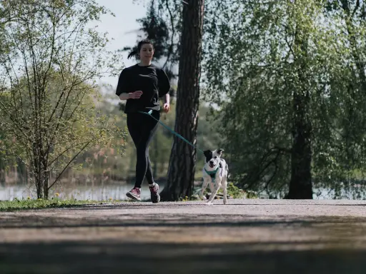 En ung kvinna och hennes hund springer längs en stig i en park. De njuter av våren och frisk luft.