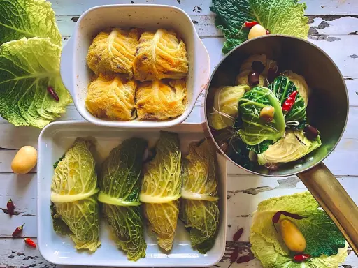 Involtini di verza pronti per essere cotti, alcuni impanati, altri legati con filo, con patate e peperoncini intorno.