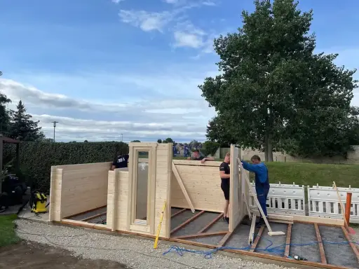 Männer bauen ein Gartenhaus. Die Montage schreitet voran, die Baugenehmigung ist hoffentlich vorhanden.