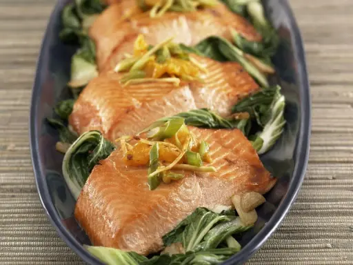 Saftiger Lachs mit Mangold, garniert mit Ingwer und Frühlingszwiebeln, auf einem dunkelblauen Teller serviert.