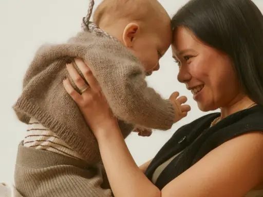 Madre y bebé se miran con ternura, frente con frente. El bebé, envuelto en un suéter de lana, muestra el apego infantil.
