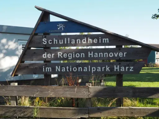 Drewniany drogowskaz "Schullandheim der Region Hannover im Nationalpark Harz" zapowiada przygodę w górach w Niemczech, być może z widokiem na szczyt Brocken.