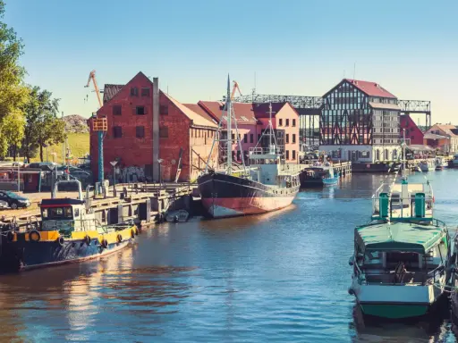 Barche ormeggiate nel porto di Klaipeda, Lituania, con edifici storici e gru sullo sfondo.