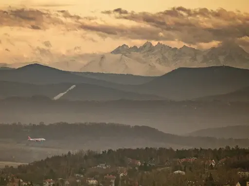 Widok na Tatry z Krakowa. Samolot leci nad mglistymi wzgórzami, a za nimi widać ośnieżone szczyty.