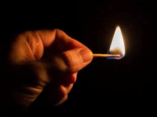 Dłoń trzyma płonącą zapałkę. Czy Polsce grozi blackout? Mały płomień symbolizuje niepewność.
