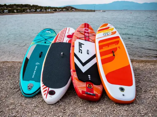 Cztery kolorowe deski SUP dla dzieci stoją na plaży, gotowe na wodne przygody.