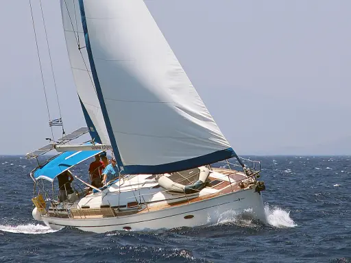 Un voilier blanc navigue sur une mer bleue agitée. L'équipage semble prendre un ris, ajustant les voiles pour mieux affronter le vent.