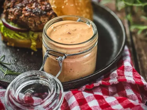 Leckere, cremige Sauce im Glas, perfekt zum schnelle Burger Sauce selber machen. Dazu ein saftiger Burger auf einem Gusseisen-Teller.