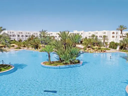 Słoneczny basen w Djerba Resort (dawniej Vincci) otoczony palmami i białymi budynkami.
