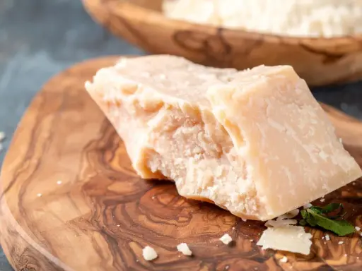 Kawałek twardego sera, przypominającego Grana Padano i parmezan, leży na drewnianej desce.