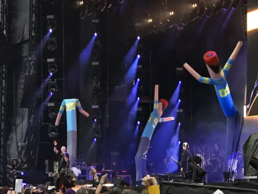 The Offspring Sverige spelar live med uppblåsbara figurer på scenen. Blå ljus och rök skapar en festlig stämning.