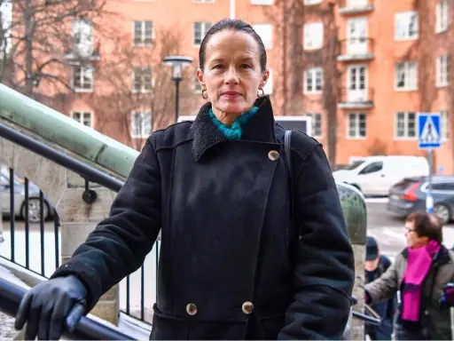 Malin Berghagen, trots att hon verkar sjuk, går uppför en trappa i en svart kappa.