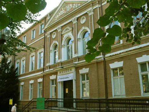 Fasada muzeum w Zielonej Górze, z napisem "MUZEUM". W pobliżu drzewa i ławka.