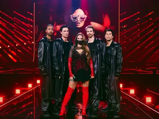 Eurovision svenska kommentatorer: artist med dansare i glänsande svarta rockar och rött, på en scen med röda ljus.