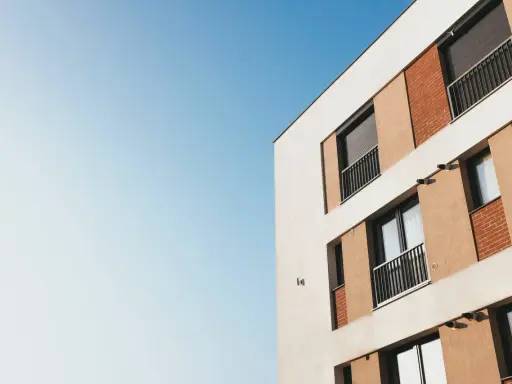 Façade d'un immeuble moderne avec balcons et volets roulants, idéal pour mettre son appartement en location. Ciel bleu clair.