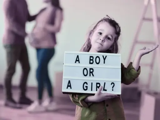 Dziewczynka trzyma tabliczkę "A BOY OR A GIRL?". Rodzice czekają na dziecko, a płeć można poznać do 20. tygodnia ciąży.