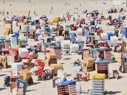 Bunte Strandkörbe säumen den Sandstrand, einige Menschen entspannen sich, andere spielen Volleyball. Ein typischer fkk strand.
