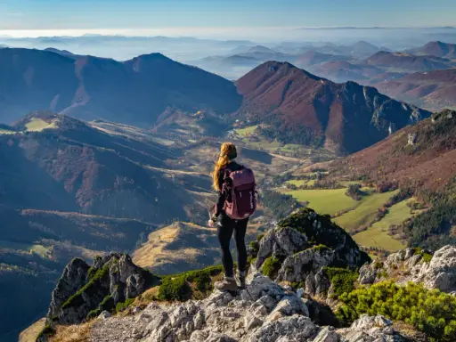 Widok na jesienne pasmo górskie Mała Fatra. Kobieta z plecakiem podziwia panoramę z kamienistego szczytu.