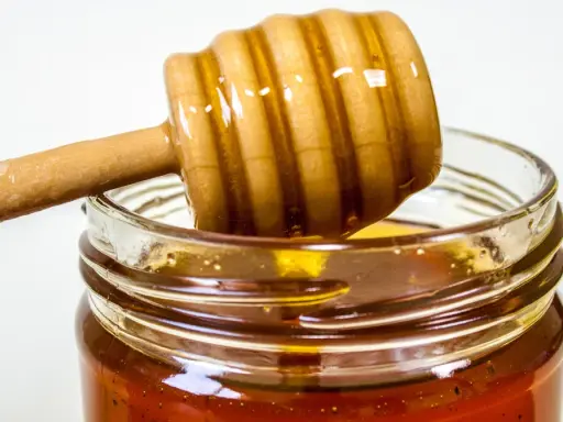 Słoik z miodem i drewniana łyżka do miodu. Naturalny antybiotyk na gardło, który pomoże złagodzić ból.