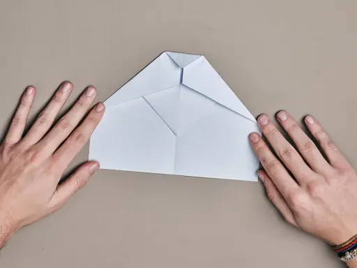 Hände falten einen weißen Papierflieger. Der runder Papierflieger nimmt langsam Form an.