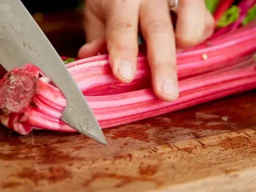 Eine Hand schneidet mit einem Messer die roten Stiele von Mangold, um ihn zuzubereiten.