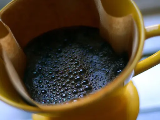 Heißer Kaffee mit Schaum in einer gelben Tasse. Ein Muntermacher, der den Unterschied zwischen Teein und Koffein verdeutlicht.