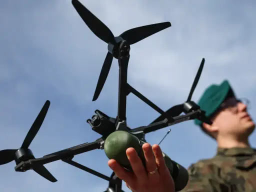 Młody dron wiek. Żołnierz w zielonym beretcie trzyma w dłoniach nowoczesny dron z kamerą i zielonym ładunkiem.