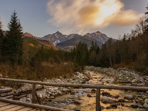 Jesienne Tatry w październiku. Drewniany mostek nad kamienistym potokiem, w tle góry i lasy.