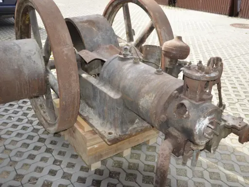 Zardzewiały silnik na gaz drzewny, z dużymi kołami, stoi na drewnianych klockach.