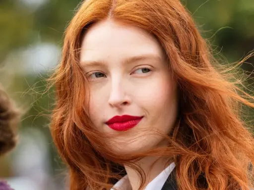 Eine Frau mit leuchtend roter haarfärbung und roten Lippen, ihr Haar weht im Wind.