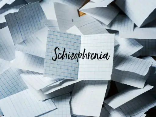Rozrzucone kartki w kratkę, na jednej napis "Schizophrenia". Obraz symbolizuje chaos myśli, objawy schizofrenii hebefrenicznej.