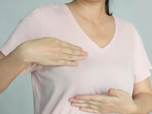 Kobieta bada swoje piersi, doświadczając bólu w piersiach, który może być związany z menopauzą.