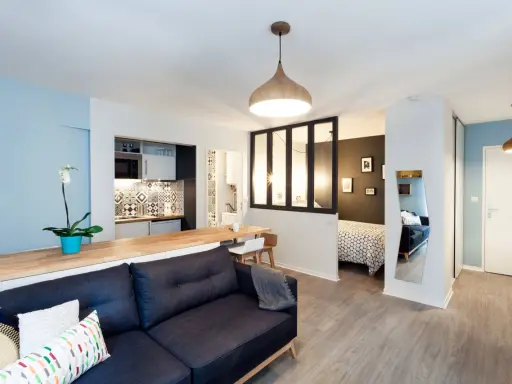 Aménagement studio 30m2 : salon cosy, cuisine moderne, chambre séparée par verrière, et coin repas.