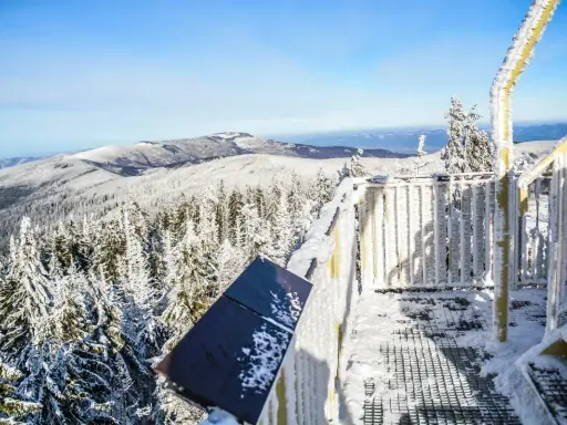 Zimowy widok z wieży widokowej na najwyższe szczyty w Beskidach. Śnieg pokrywa drzewa i balustrady.