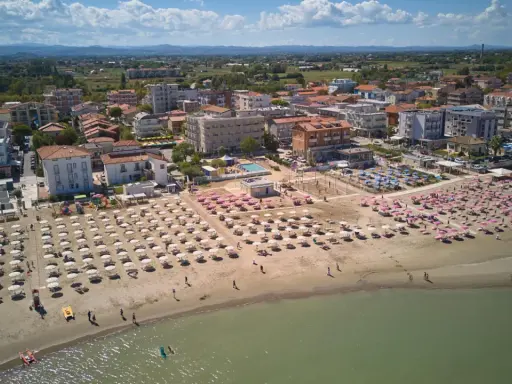 Vista aerea di una spiaggia affollata con ombrelloni rosa e bianchi, hotel e case nel centro storico di Torre Pedrera.