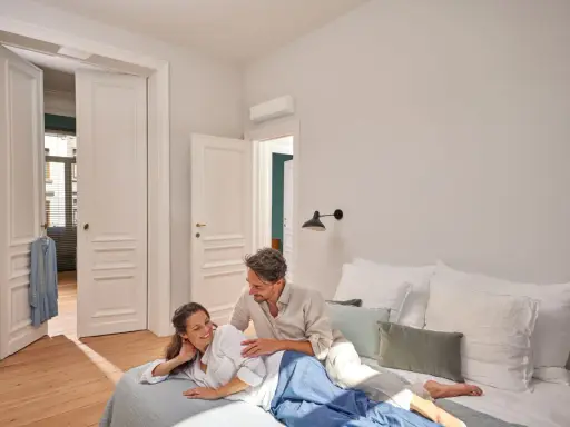Pareja relajada en la cama, disfrutando de un ambiente fresco gracias al aire acondicionado, ideal para un buen sleep.