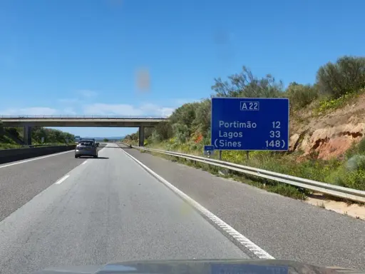 Autobahn A22 in Portugal. Ein Auto fährt auf der rechten Spur, vorbei an einem Schild mit Zielen wie Portimão und Lagos.