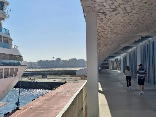 Una nave da crociera attracca nel porto di Leixões, Portogallo. Due persone passeggiano sotto una moderna tettoia con un soffitto decorato.