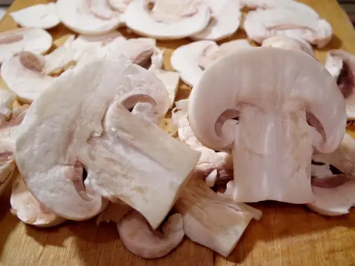 Pokrojone pieczarki na desce. Czy można jeść surowe pieczarki? Tak, te białe są gotowe do spożycia na surowo.